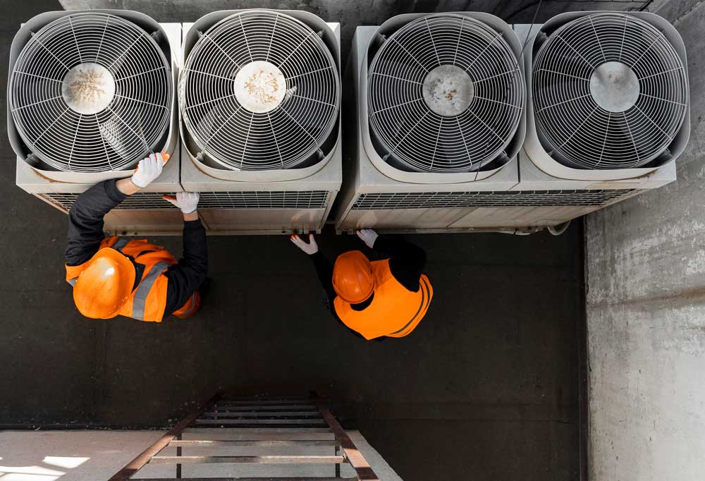 Zwei Techniker in Warnschutzkleidung warten Dachventilatoren einer Lüftungsanlage